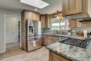 Una cocina con armarios de madera, un refrigerador de acero inoxidable, una encimera de mármol y un tragaluz.