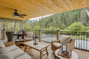 A covered outdoor deck with wicker furniture, a ceiling fan, and a view of a forested area. - Pool & Dual Decks! Modern Trinity River Retreat (Douglas City)