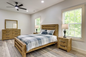 Une chambre Ă coucher avec un lit, des tables de chevet en bois, un ventilateur de plafond et des fenĂȘtres Ă©quipĂ©es de stores.