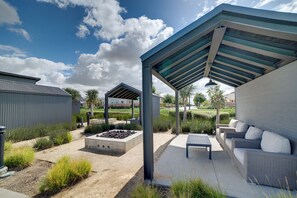 Een overdekt terras met een bank en tafel, een betonnen plantenbak en een metalen constructie.