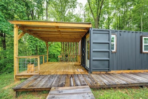 A wooden deck with a pergola, a small table with chairs, and a grey container-like structure.