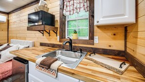 A compact kitchen with a sink, wooden countertop, and a window with curtains. - Tiny Cabin Nature Retreat Near Blue Rock (Cumberland)
