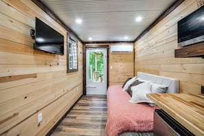 A wooden interior with a bed, a TV, and an air conditioning unit.