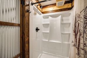Une douche avec un cadre en bois, une pomme de douche en métal et un mur recouvert de carreaux blancs.
