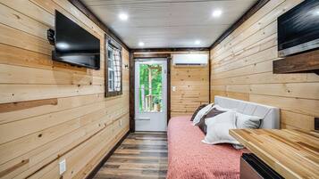 A wooden interior with a bed, a TV, and an air conditioning unit.