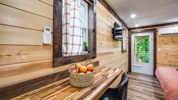 A wooden interior with a wooden bench, a basket of fruit, a chair, and a bed with a pink blanket. - Tiny Cabin Nature Retreat Near Blue Rock (Cumberland)
