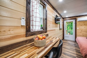Un interior de madera con un banco de madera, una cesta de fruta, una silla y una cama con una manta rosa.