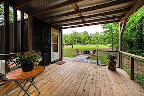Une terrasse en bois avec une table et des chaises, une porte donnant sur un espace abrité et une vue sur une cour verdoyante.
