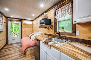 A compact room with a bed, a sink, a microwave, and a window with curtains.