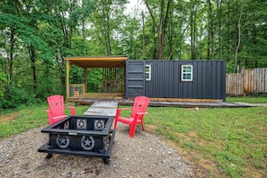 Une cabane avec une terrasse, deux chaises rouges et une table décorée de motifs en forme d’étoiles.