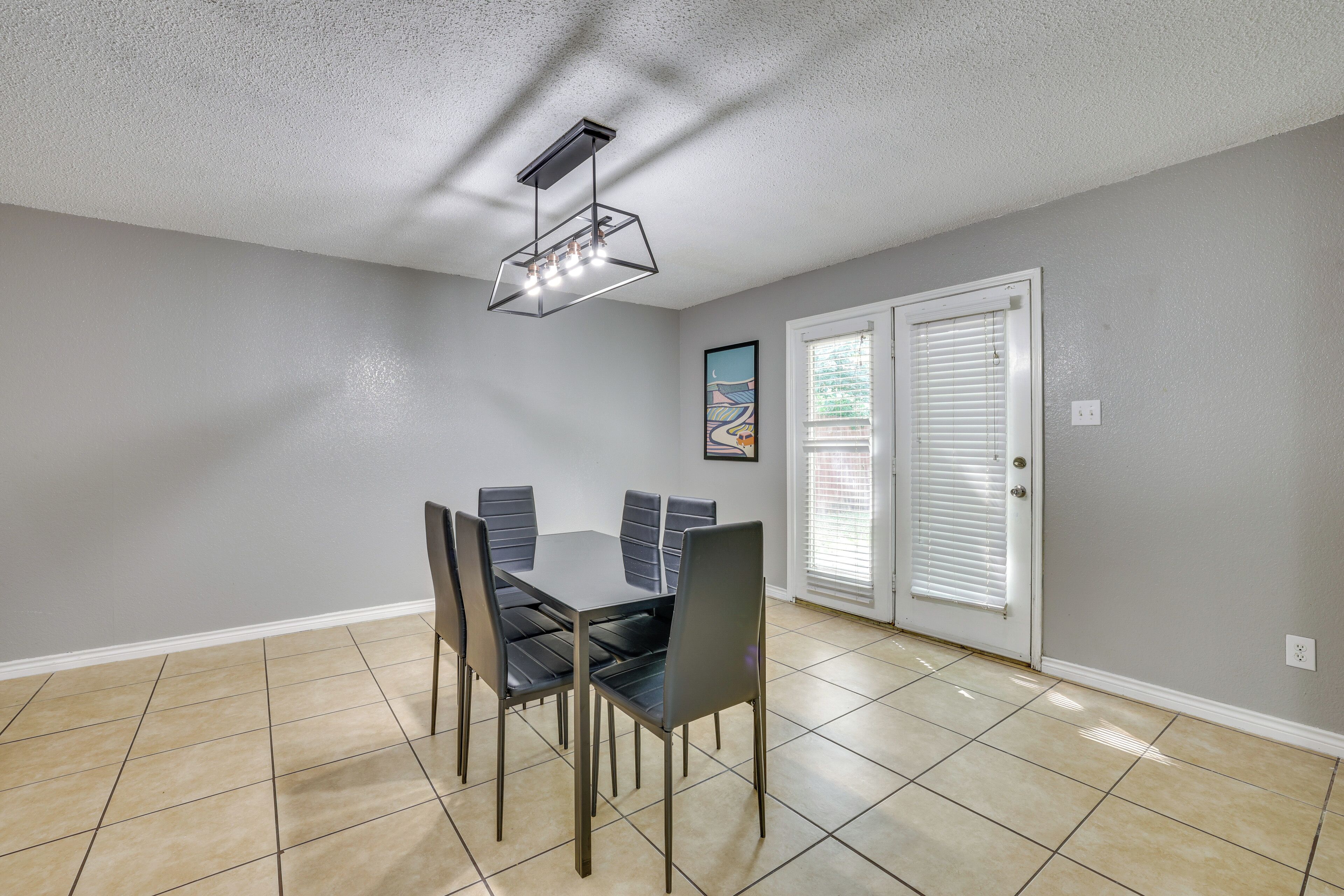 A dining area with a table and chairs, a ceiling light fixture, and a door with blinds.