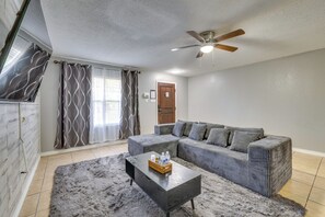 Una sala de estar con un sofá modular, una mesa de centro, un ventilador de techo y una puerta al fondo.