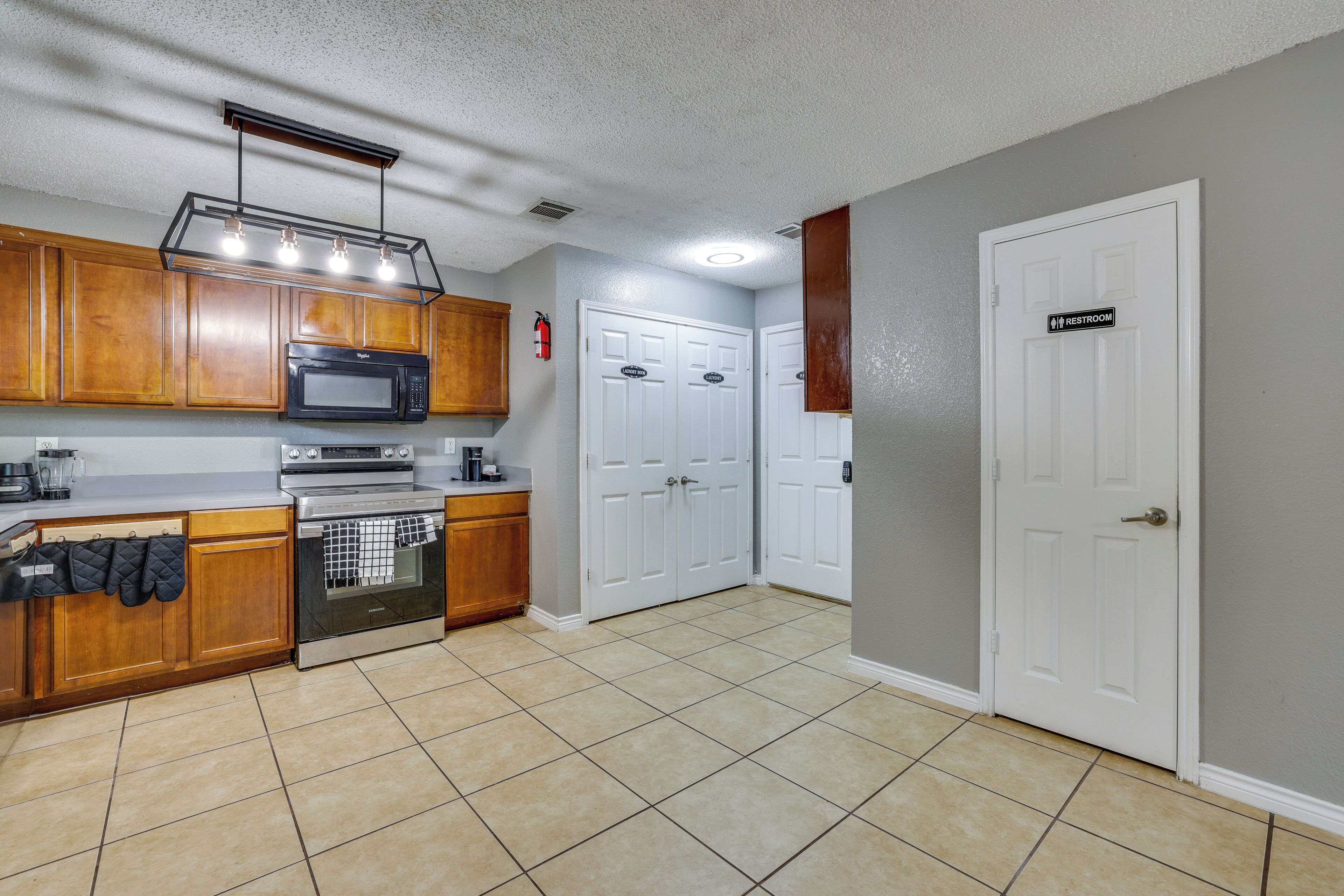 A kitchen with wooden cabinets, a microwave, an oven, and a dishwasher. There are two white doors, one marked 'Restroom.'