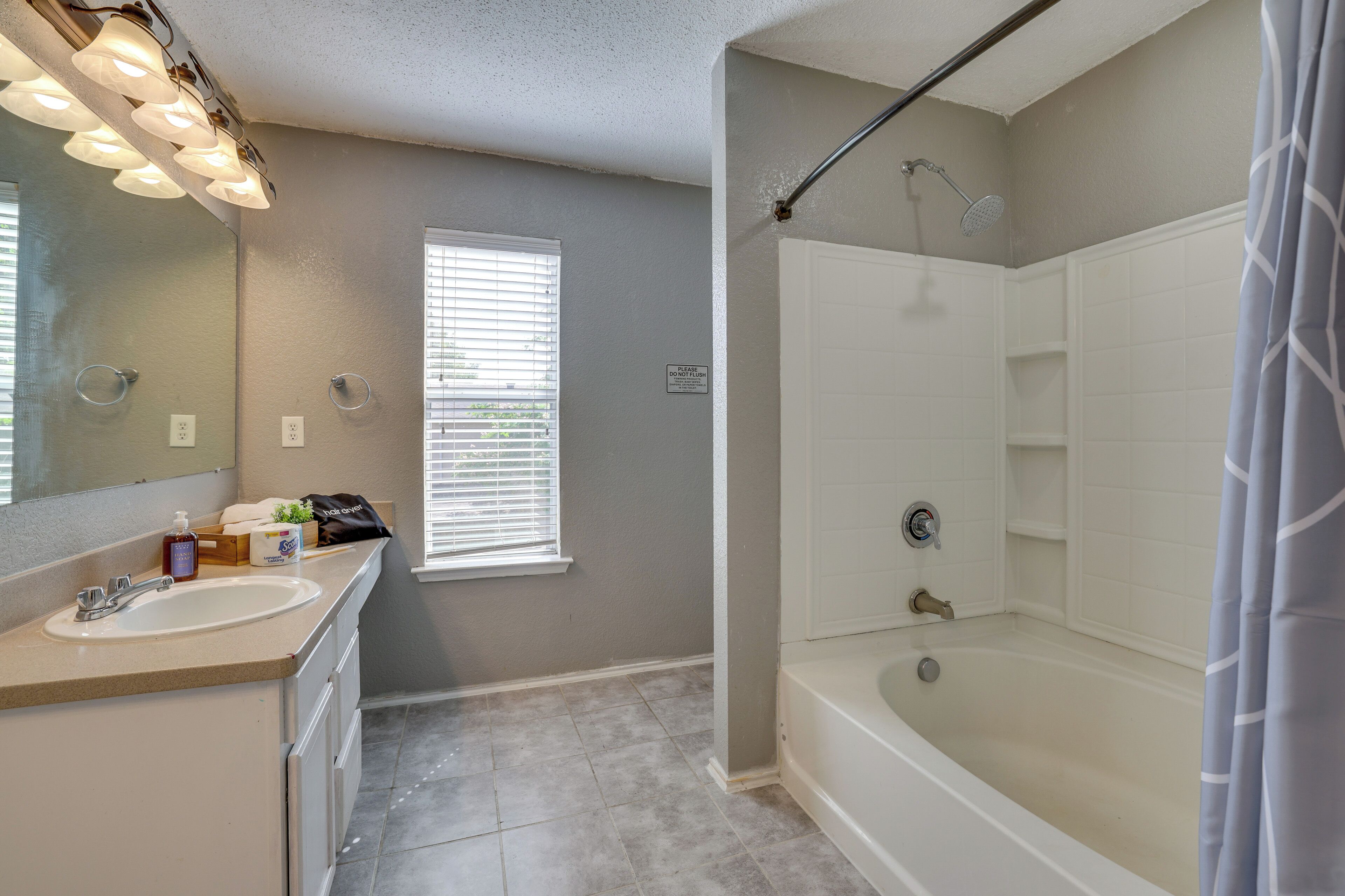 A bathroom with a sink, mirror, shower, and a window.