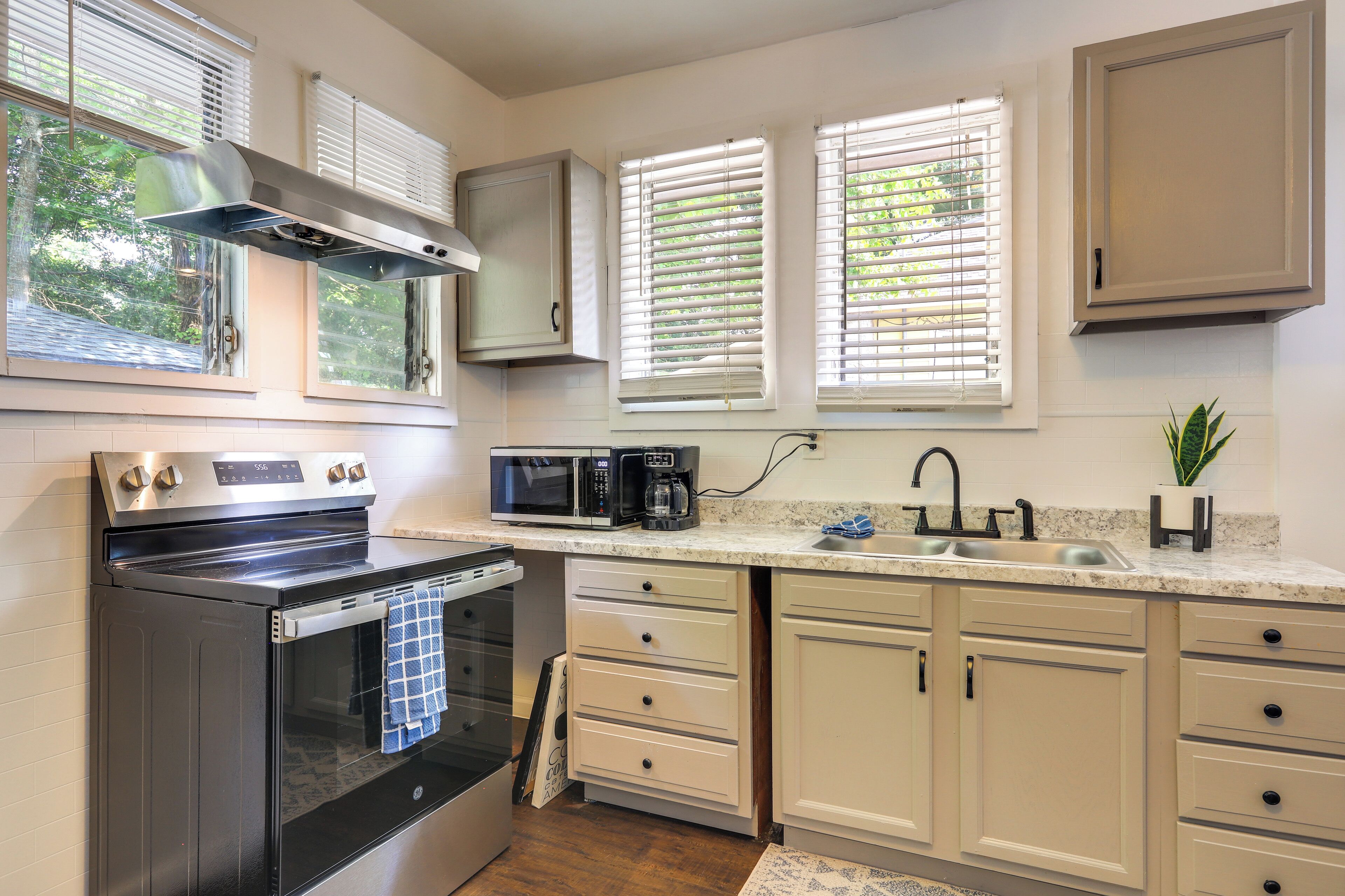 A kitchen with a built-in oven, microwave, and coffee maker, with white cabinets and a window with blinds.