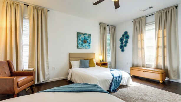Ein Schlafzimmer mit zwei Betten, einem Deckenventilator, einer Bank, einem Sessel und einem Gemälde an der Wand.
