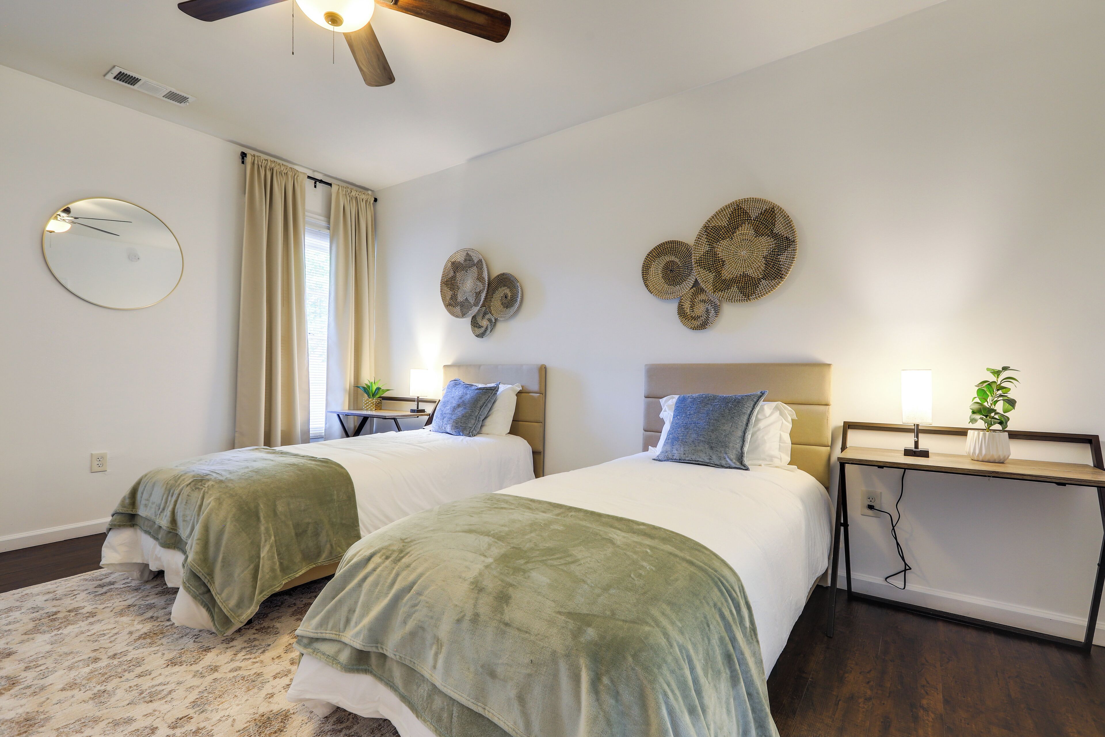 Une chambre d’hôtel avec deux lits, un ventilateur de plafond, une horloge murale ronde et des œuvres d’art décoratives accrochées au mur.