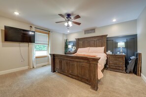 A bedroom with a bed, a TV, a ceiling fan, a dresser, and a nightstand.