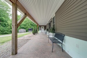 Une véranda avec un banc, des piliers en bois et une vue sur une maison et la verdure.