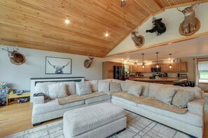 A spacious living room with a large sectional sofa, wooden ceiling, and mounted animal heads.