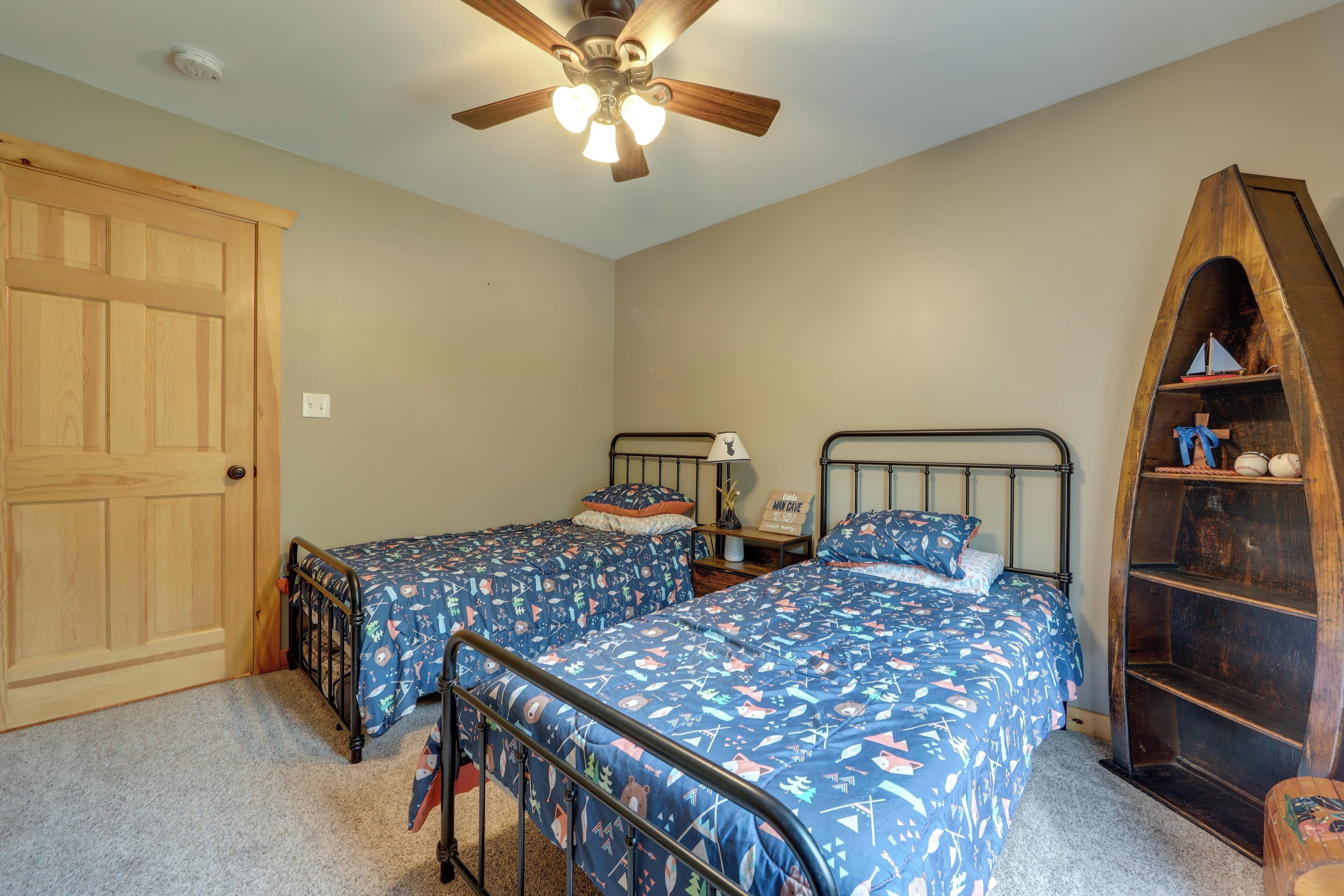 A bedroom with two beds, a wooden door, a ceiling fan, and a bookshelf.