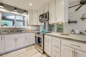 A modern kitchen with white cabinets, stainless steel appliances, a window, and a ceiling fan.
