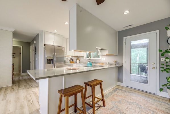 A modern kitchen with a large island, wooden stools, and a view to the outside.