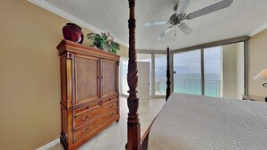 A bedroom with a four-poster bed, a wooden dresser, a ceiling fan, and a view of the ocean. - The Pearl of Navarre #1502 | Gulf Front + Resort Amenities (Navarre Beach)