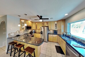A modern kitchen with a central island, bar stools, a refrigerator, and a window with a view.