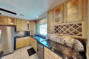 A kitchen with wooden cabinets, a stainless steel refrigerator, a black countertop, and a window providing natural light.