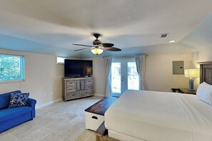 A bedroom with a bed, a ceiling fan, a TV, a dresser, and a window.