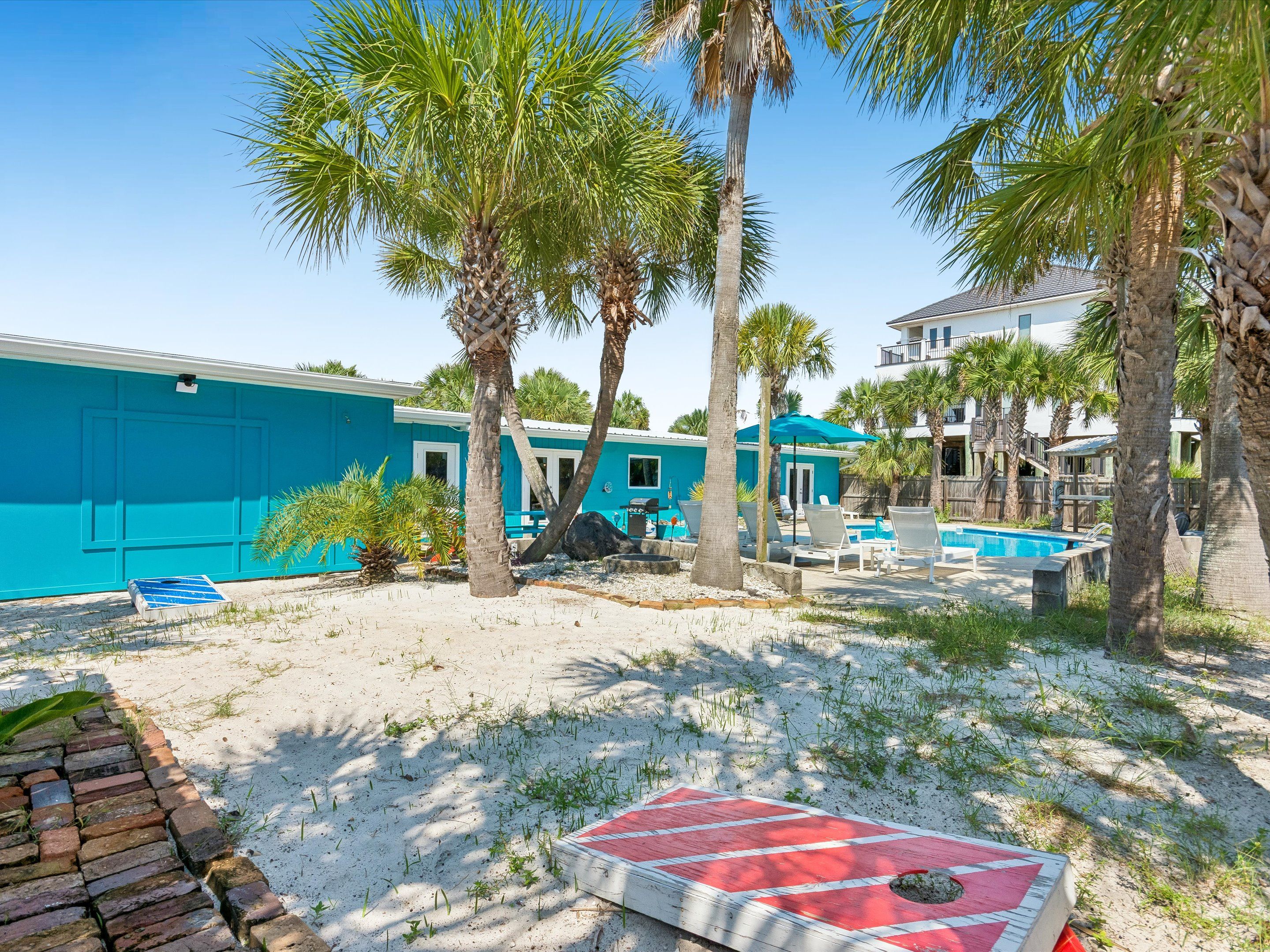 Ein Anwesen direkt am Strand mit Pool, Palmen und einem blauen Gebäude.