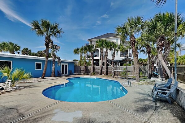 A swimming pool with a curved edge, surrounded by palm trees and a wooden fence.