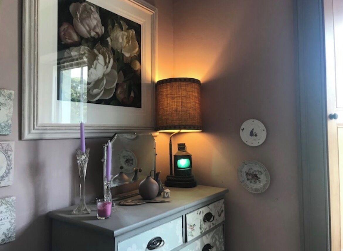 Et værelse med et blomsterbillede i ramme, en lampe, en vase med et lys og en vintage radio.