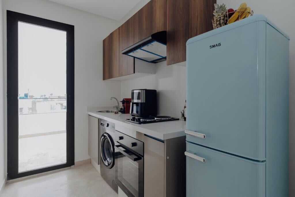 Eine moderne Küche mit Waschmaschine, Kaffeemaschine und einem blauen Kühlschrank.