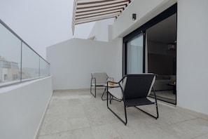 A balcony with two chairs, a glass door leading inside, and a view of buildings in the background. - The Shelter (Casablanca)