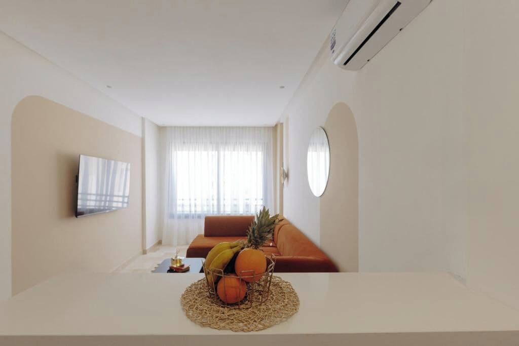 A modern living room with a sofa, a TV, and a fruit bowl on a table.