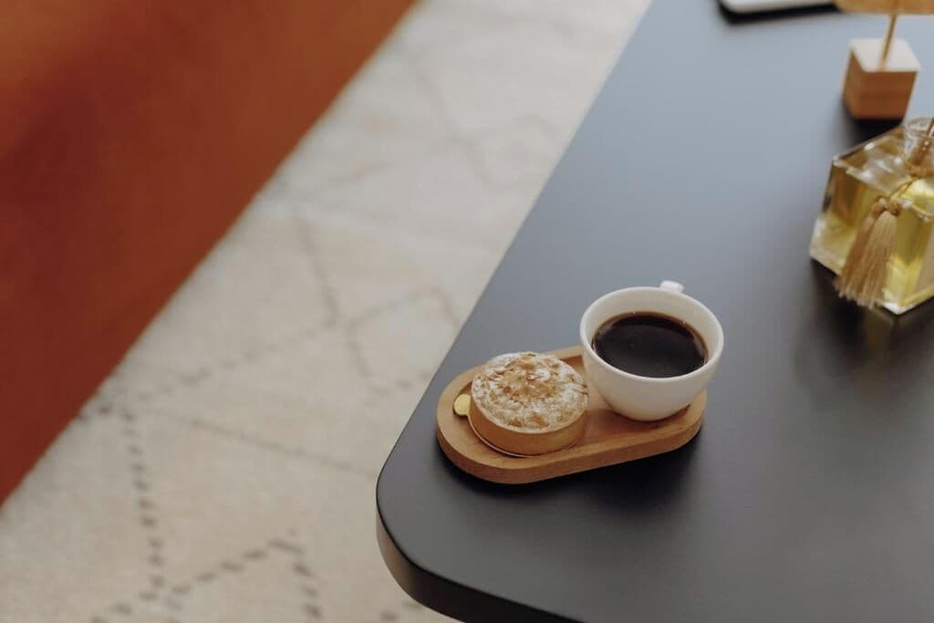 Una mesa con una taza de café, un pastel y dos frascos de perfume.