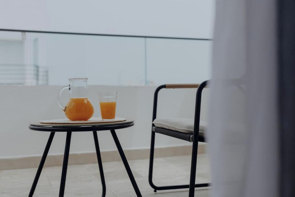 Un balcón con una mesa, una silla, una jarrón y un vaso de jugo de naranja.