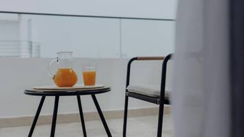 Un balcón con una mesa, una silla, una jarrón y un vaso de jugo de naranja.