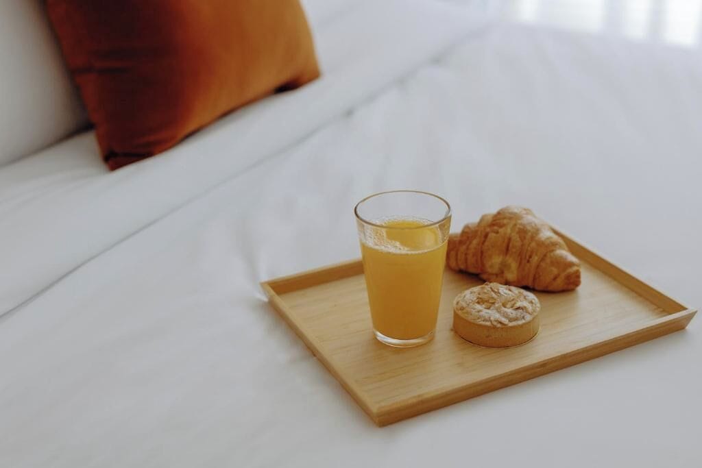 A tray with a glass of orange juice and a croissant on a bed.