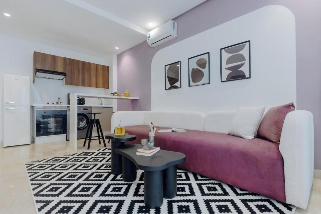 A modern living room with a sofa, a coffee table, and a kitchen area in the background.