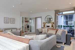 A modern living room with a sofa set, a bookshelf, a dining area, and a large window. - Stunning Notting Hill Flat (London)