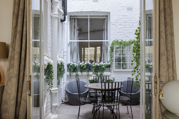 A white brick exterior, a glass door entrance, a round table with chairs, and a window with hanging plants. - Stunning Notting Hill Flat (London)