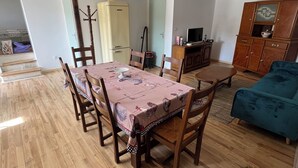 Ruokailutilassa on puinen pöytä ja tuolit, sininen sohva, puinen kaappi ja vanhanaikainen jääkaappi.