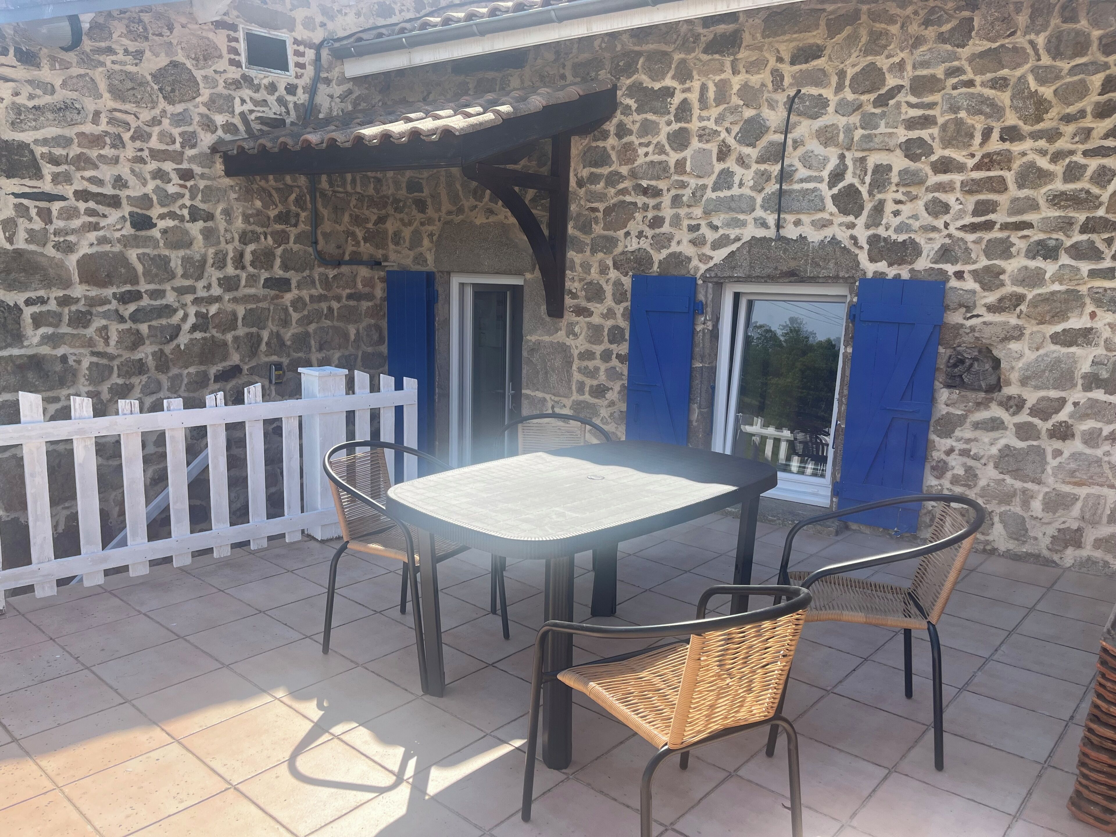 A stone building with a tiled patio, a white picket fence, and a table with chairs.