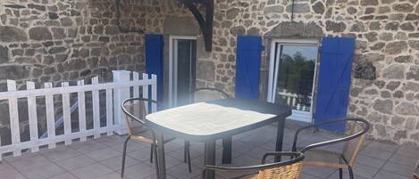 Un edificio de piedra con un patio empedrado, una cerca de piquetes blancos y una mesa con sillas.