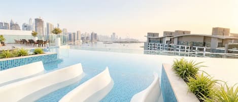 A rooftop infinity pool with a city skyline view, modern architecture, and outdoor seating.