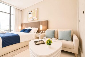A hotel room with a bed, a sofa, a coffee table, a chessboard, and a painting on the wall. - Rentico | Infinity Pool Studio on Palm Jumeirah (Dubai)