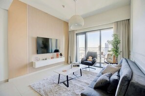 Ein modernes Wohnzimmer mit Flachbildfernseher, einer Couch, einem Couchtisch und einem großen Fenster mit Blick auf die Stadt.